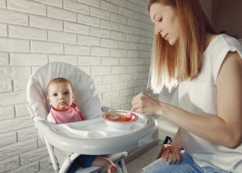 Baby eating. Mother feeds the baby. Little child in a kid's chair.